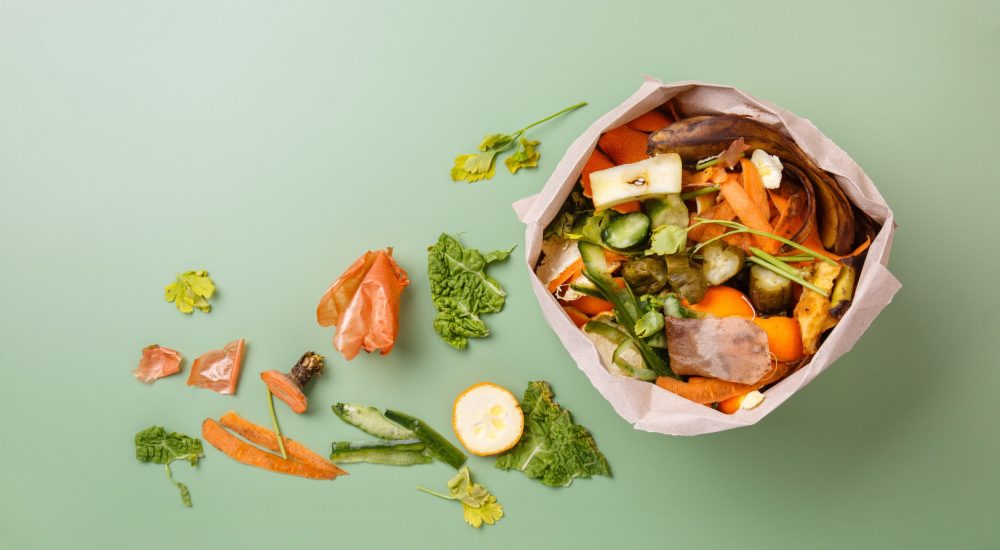 Sorted kitchen waste in paper eco bag on green background. Compo
